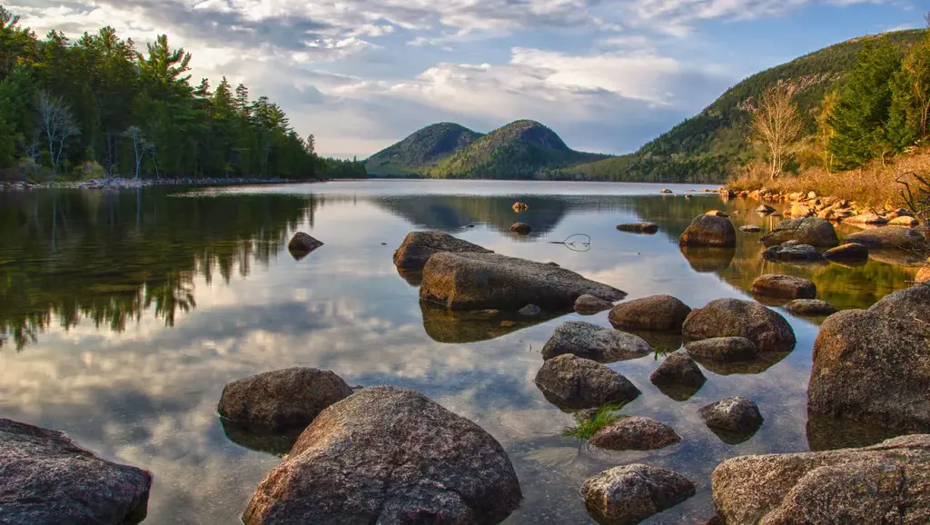 Reflection of tall trees and rolling mountains in the still waters of Jordan Pond in Acadia National Park
